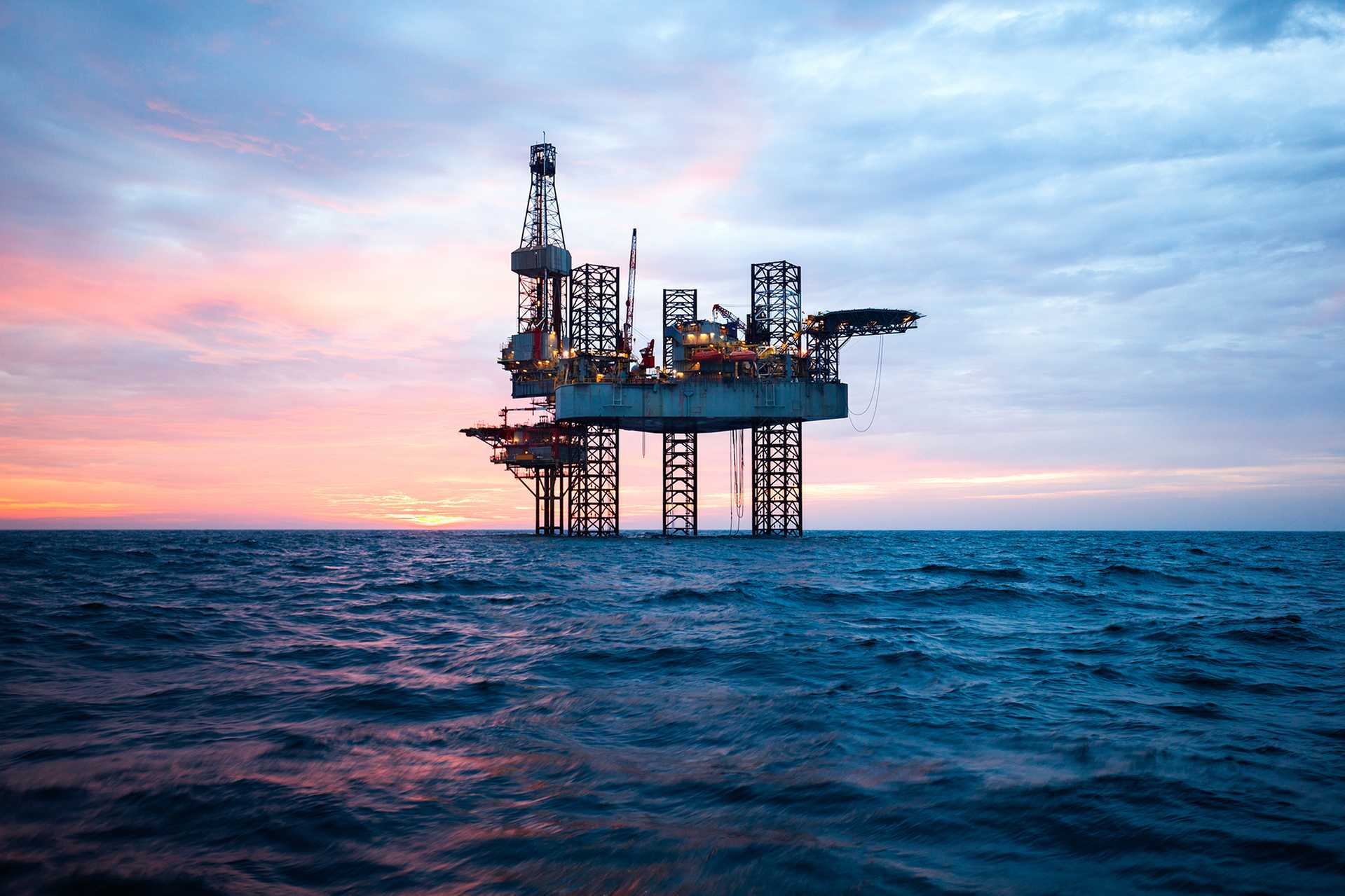 Offshoreinstallasjon på flatt hav med farget himmel.